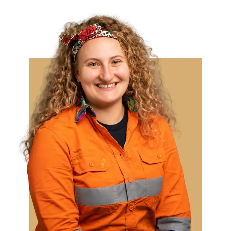 Studio portrait of Louise Azzopardi smiling, wearing an orange high-vis shirt against a grey backdrop